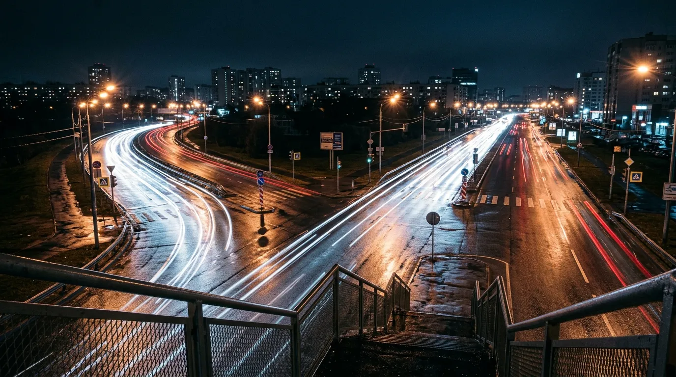 Foto nocturna de larga exposición de una avenida que se bifurca en dos, con las estelas de luz de los coches dividiéndose en el cruce